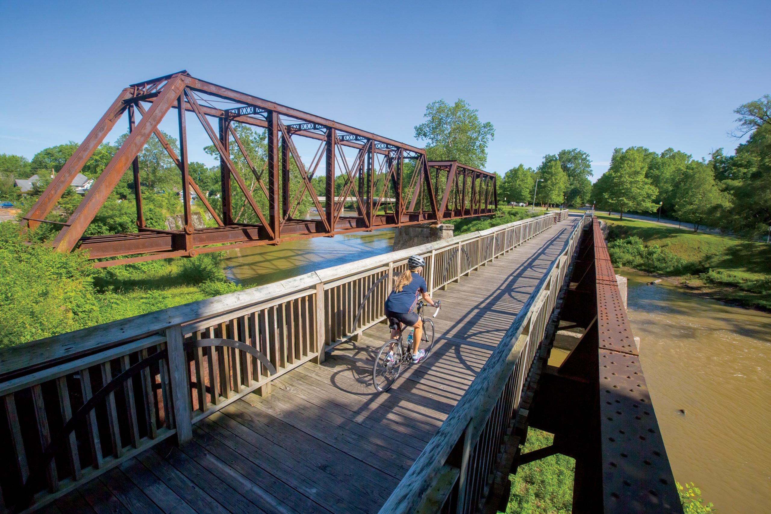 Woman on bicycle on a bridge across a bridge which crosses the White River along the Cardinal Greenway in Muncie, Indiana