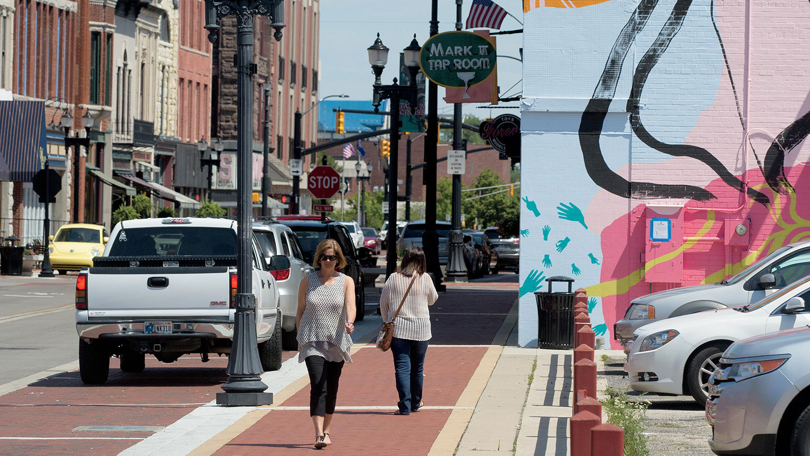 Woman walking downtown Muncie, Indiana near a colorful mural on the side of a building