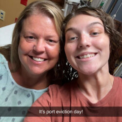 A mother and daughter smile together for a selfie at the hospital before the mother’s chemotherapy port removal, five years after her breast cancer diagnosis.